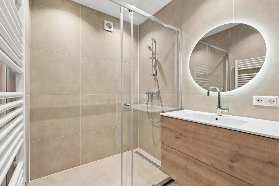 Badkamer met inloopdouche, houten wastafelmeubel en ronde spiegel met verlichting